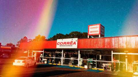 Foto frontal da Corrêa Materiais Elétricos. Na parte superior do prédio uma fachada vermelha com placa uma placa branca com Corrêa em vermelho.