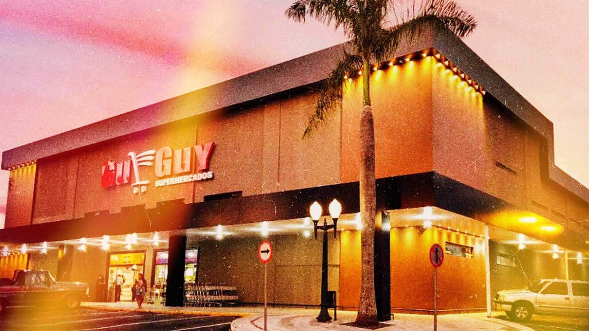 Foto da Guguy supermercados no final da tarde com as luzes ligadas.