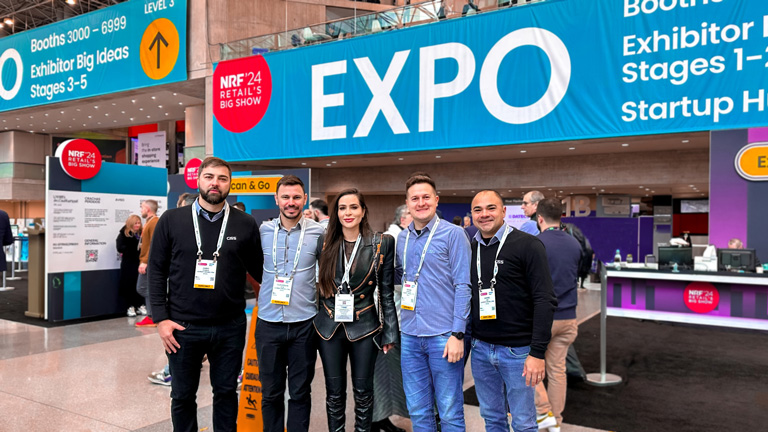 Colaboradores da CISS posicionados um ao lado do outro em frente a entrada da NRF 2024.