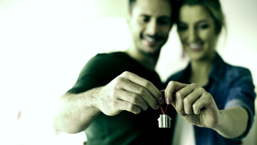 Casal segurando a chave da casa própria, olhando pra frente.